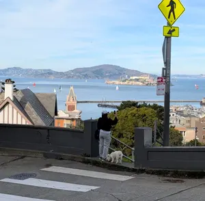 A woman with her dog taking a picture of Alcatraz