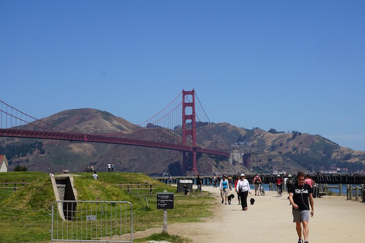 Pedestrians enjoying the wide path of Crissy Field in front of the Golden Gate Bridge